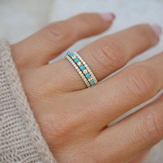 a woman's hand with a diamond and turquoise ring on her left hand, wearing a sweater