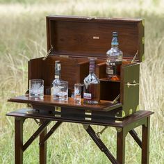 an open wooden box with liquor bottles in it on top of a table next to grass