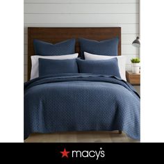 a bed with blue bedspread and pillows on top of it, next to a night stand