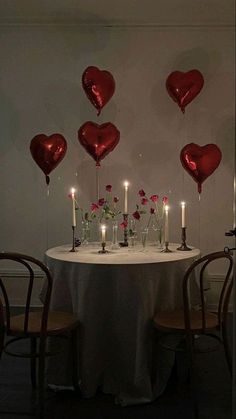 a table topped with lots of red heart shaped balloons and candles in front of it