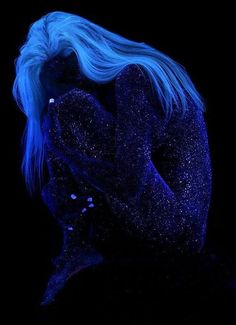 a woman with blue hair is sitting in the dark and has her hands on her face