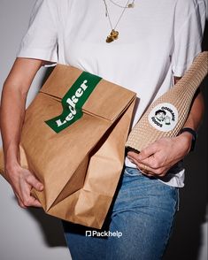 a person holding a brown paper bag with a green label on it and a white t - shirt