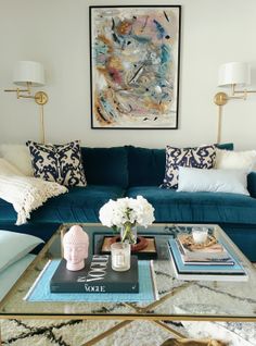 a living room with blue couches and white pillows on the coffee table in front of a painting