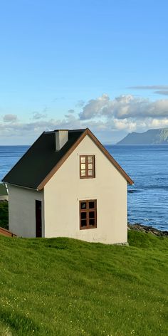 a small white house sitting on top of a lush green field next to the ocean