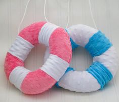 two stuffed toys are hanging from strings on a white tablecloth covered surface, one is pink and the other is blue