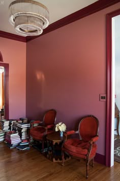 two red chairs sitting next to each other on a hard wood floor in front of a pink wall