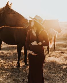 a pregnant woman standing in front of horses