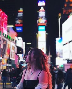 a woman standing in the middle of a busy city street at night with neon lights