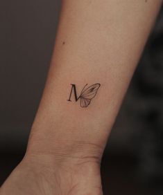 a small butterfly tattoo on the wrist is shown in black and grey ink, with an upper letter m