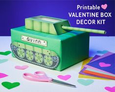 a green box with a pink pair of scissors next to it and some paper hearts