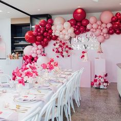 a table set up for a party with pink and white balloons hanging from the ceiling