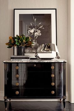 a black and white dresser with flowers on top in front of a framed photo above it