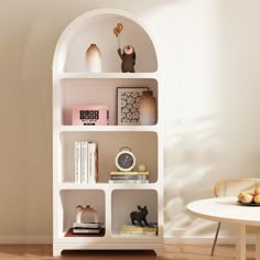 a white book shelf with books on top of it in a living room next to a table