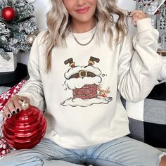 DESCRIPTION Retro Santa Going Down The Chimney Christmas Sweatshirt Celebrate the holiday season in style with this festive women's Christmas sweatshirt! Designed with a cheerful holiday theme, this cozy sweatshirt is perfect for all your seasonal activities--from decorating the tree to sipping hot cocoa by the fire. Made from soft, premium fabric, it's designed to keep you warm and comfortable while spreading holiday cheer. Whether you're attending a Christmas party, going on a holiday shopping Cozy Long Sleeve Christmas Tops, Cozy Long Sleeve Holiday Tops, Casual Cozy Christmas Top, Casual Christmas Sweatshirt For Festive Occasion, Casual Christmas Festive Sweatshirt, Christmas Long Sleeve Tops With Cozy Fit, Festive Winter Crew Neck Top, Casual Christmas Sweatshirt, Cozy Crew Neck Holiday Tops