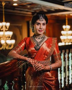 a woman in an orange and gold sari poses for a photo with chandeliers