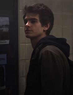 a young man standing in front of a urinal with his head turned to the side