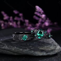 two rings sitting on top of a rock next to each other with green stones in the middle