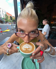 a woman with glasses is drinking from a cup in front of her face and looking at the camera