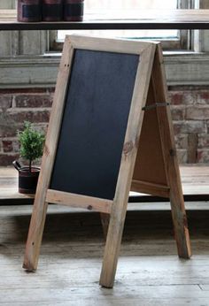 a wooden sign sitting in front of a window next to a potted green plant