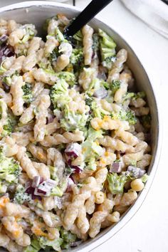 a pasta salad with broccoli and cheese in a white bowl on a table