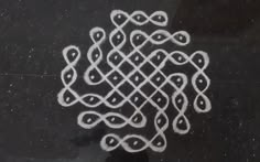 an intricate design is drawn in white chalk on a black surface, with small dots at the center