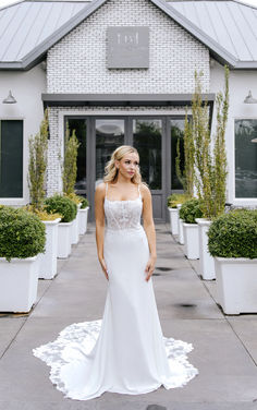 a woman standing in front of a building wearing a white wedding dress with an open back