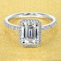 an emerald cut diamond ring with pave diamonds around the band on a gold background