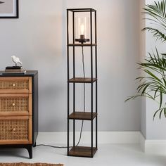 a tall black metal shelf with two candles on it next to a potted plant