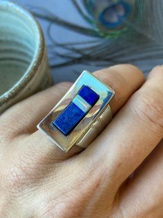 This wonderful statement ring was made by the popular design company, Desert Rose Trading Company. It has Western and Tribal design elements and has been crafted in sterling silver with lapis lazuli and synthetic opal inlay. The ring has wonderful coverage on the finger and would likely fit up to a full size smaller than what's listed. The total weight is 13 grams and the face measures one inch long. Inside the ring is stamped DTR China 925. The ring measures a US size 8  To view similar items return to our shop here- https://www.etsy.com/shop/Luere Your jewelry will come beautifully packaged and ready to give as a gift. Each piece comes in a hand decorated brown paper gift box wrapped with love! For multiple purchase orders - Please let me know in the "notes to seller" upon checkout if yo Modernist Blue Gemstone Jewelry, Blue Modernist Jewelry With Polished Finish, Modernist Blue Jewelry With Polished Finish, Modern Sterling Silver Opal Ring Gift, Modern Sterling Silver Opal Ring For Gift, Modernist Rings With Inlay For Gift, Modernist Rings With Inlay Perfect For Gifts, Modern Silver Ring With Inlay, Modern Silver Rings With Inlay