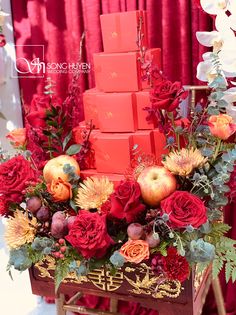 an arrangement of flowers, apples and candles in a wooden cart with red curtains behind it