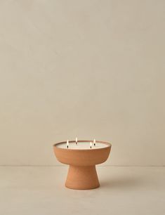 three lit candles in a clay bowl on a white surface with no one around it