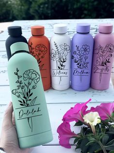 four different colored water bottles sitting on top of a white table next to pink flowers