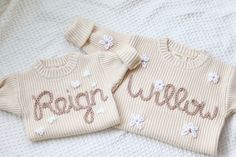 two sweaters with the word reign written on them are laying on a white blanket