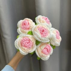 a hand holding a crocheted bouquet of pink and white flowers in front of a curtain