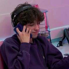 a young man wearing headphones while talking on a cell phone in front of a computer