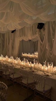 a long table covered in lots of white chairs and lit candles on top of it