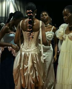 several women in dresses are standing together and looking at something on the floor behind them