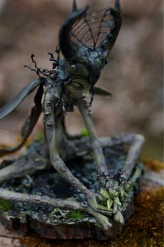 a statue of an insect on top of a piece of wood with moss growing around it