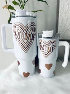 two white coffee mugs with brown hearts and the words mama on them are next to a potted plant