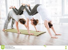 three women are doing yoga in the middle of a room with large windows and wooden floors