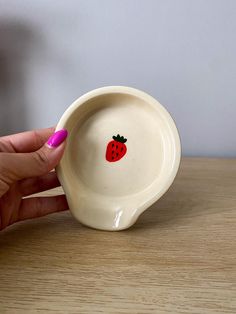 a hand is holding a small bowl with a strawberry painted on the front and side