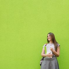 a girl standing in front of a green wall holding a book and smiling at the camera