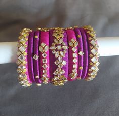 Hey lovely people... Thanks for visiting my shop. Here I have a  very beautiful  silk thread bangles heavily embellished with glass kundans in magenta pink and royal purple colours. Very royal in look. A set of 9 bangles for one hand.  You will receive 18 bangles for both hands.  A must have combo in your wardrobe. Kindly note that the actual colours and sizes of embellishments may vary slightly due to computer screen resolution and I truly hope that you do like my handmade products just as much Pink Bangles, Silk Thread Bangles Design, Wedding Bangles, Royal Purple Color, Hand Jewellery, Thread Bangles Design, Bridal Gift Wrapping Ideas, Purple Set, Kundan Bangles