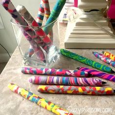 many colorful pens are lined up in a glass on a counter top next to a lamp