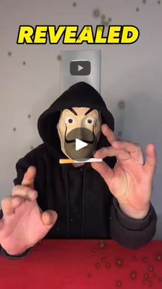 a person in a black hoodie is holding a paper mask with the words revealed on it