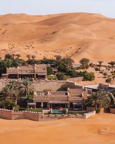 an aerial view of a desert resort surrounded by palm trees and sand dunes, with houses in the foreground