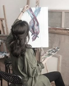 a woman is sitting in front of an easel holding up a piece of art