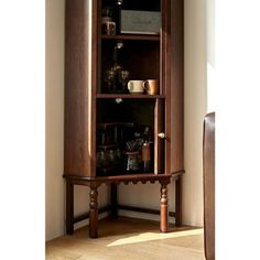 a tall wooden cabinet with glass doors and shelves on the top, in front of a white wall