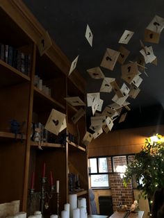 some books are flying in the air above a table and shelves with candles, vases and other items