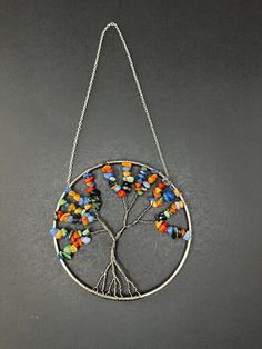 a tree of life with multicolored beads hanging from a chain on a gray surface